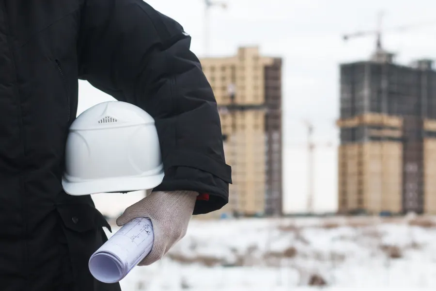 Engineer holding a hard hat and rolled plans at a construction site