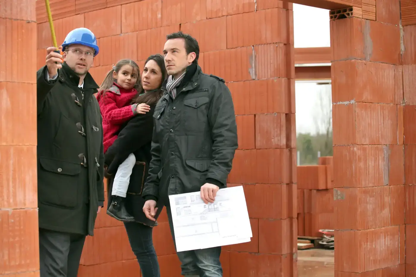 Inspector in a hard hat walking a family through their home while the brick walls go up